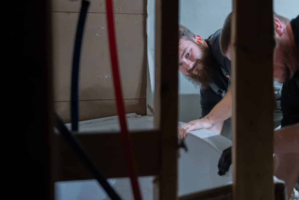 Two plumbers removing a tub unit for a bathroom remodel.