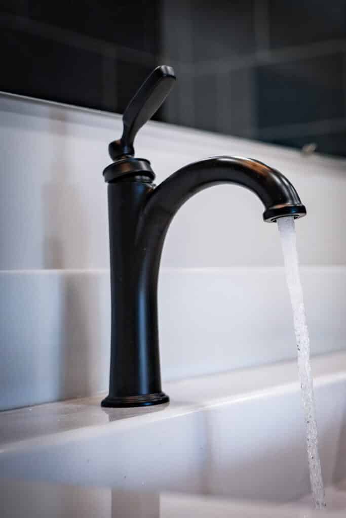 Matte black bathroom faucet with water running into a white vanity sink.