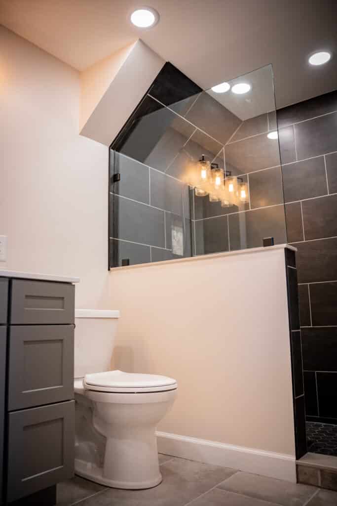Frameless glass shower partition with dark gray wall tile and a decorative shower niche in a remodeled bathroom.