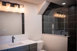 Finished bathroom remodel with gray vanity, white countertop and dark tiled walk-in shower.
